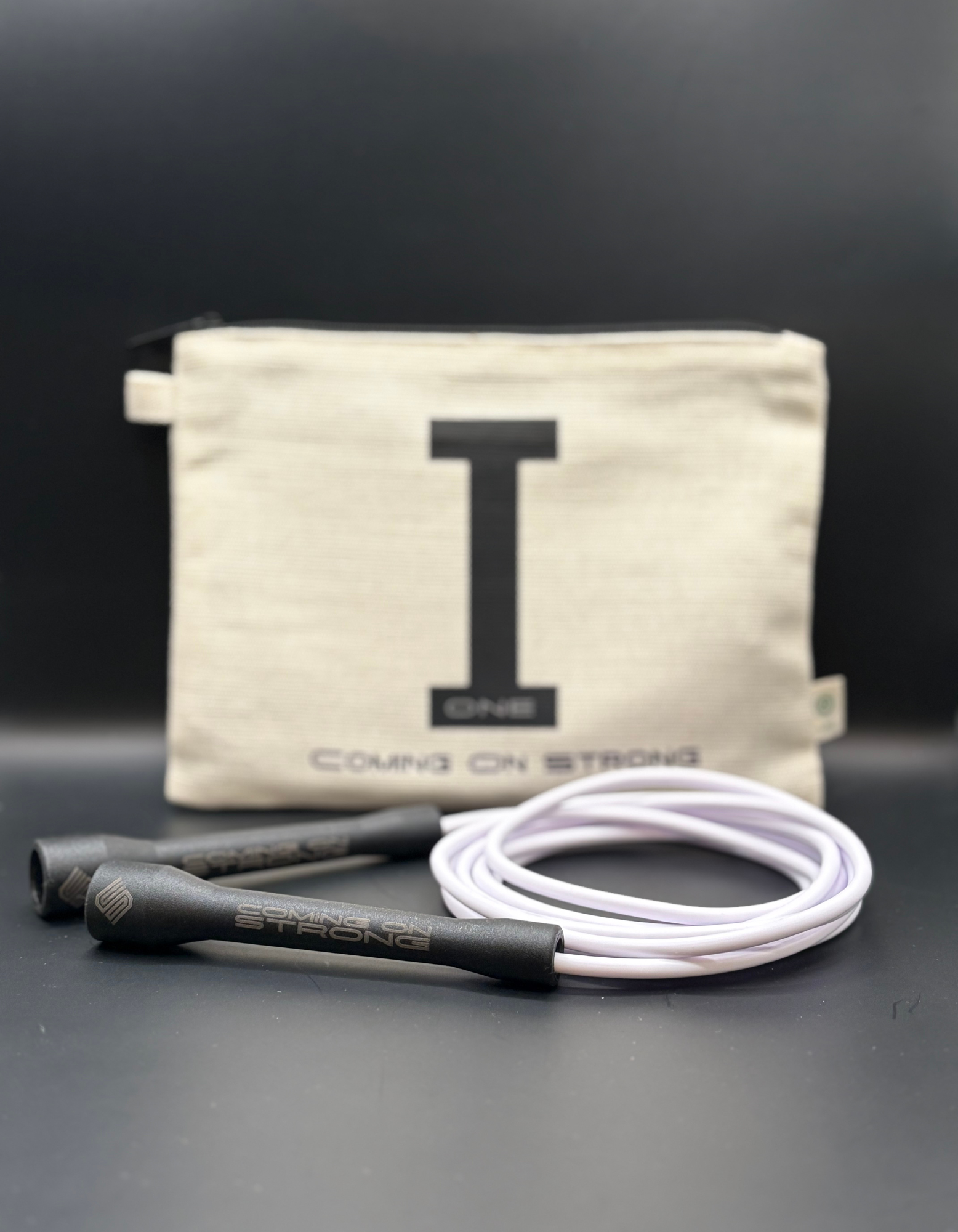 White Coming On Strong jump rope with tan hemp carry bag and black handles.